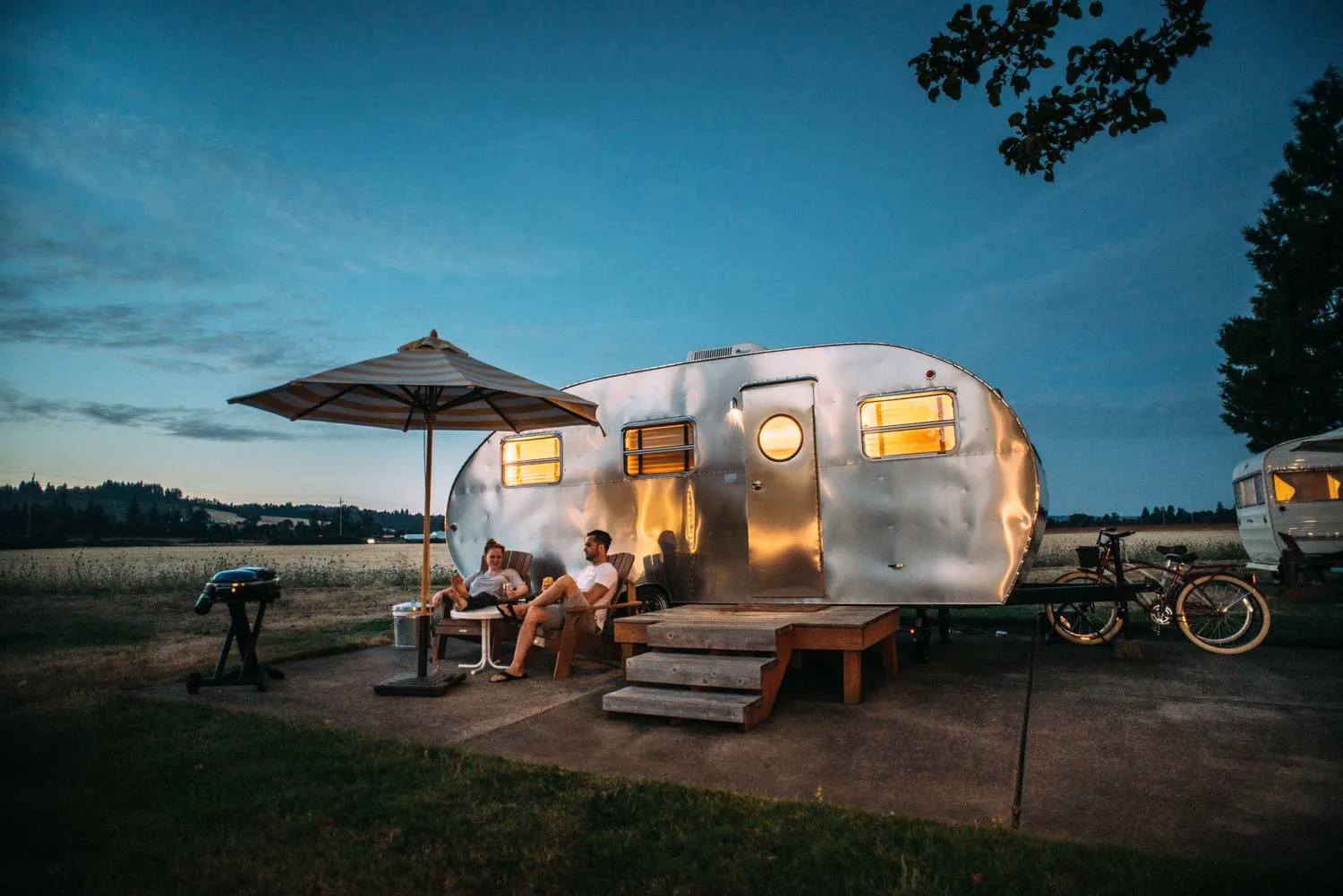 Retro trailer with an awning and chairs set up at dusk