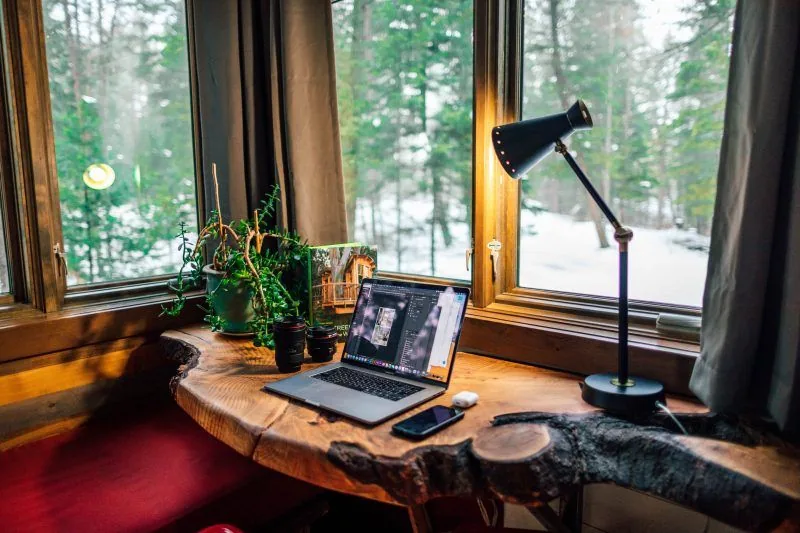 Laptop and phone on a wooden desk by a window overlooking snowy woods