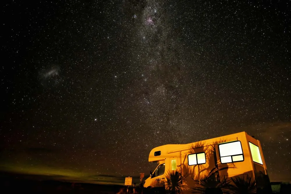 RV with lit windows parked under a starry night sky